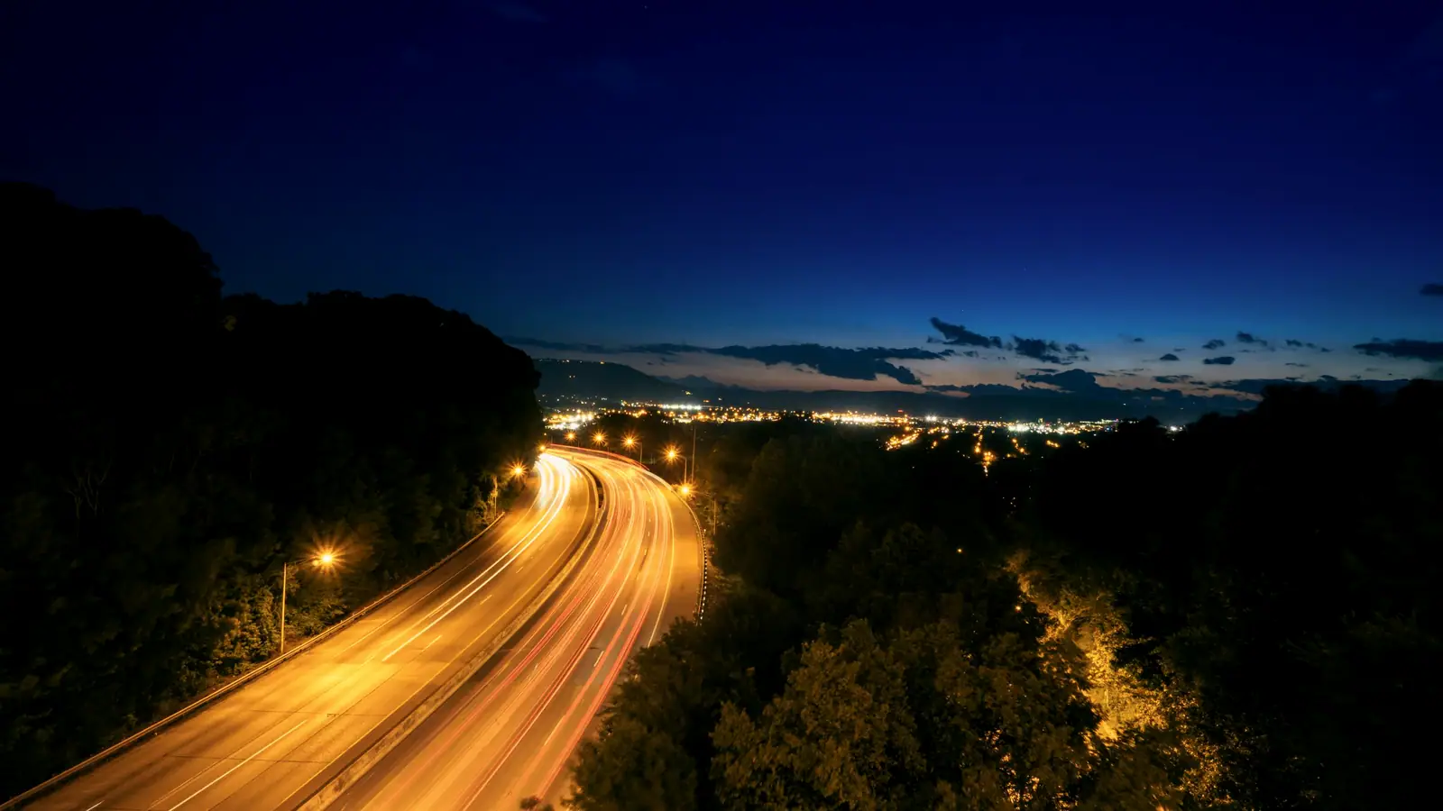 Highway light trails leading to a city at blue hour