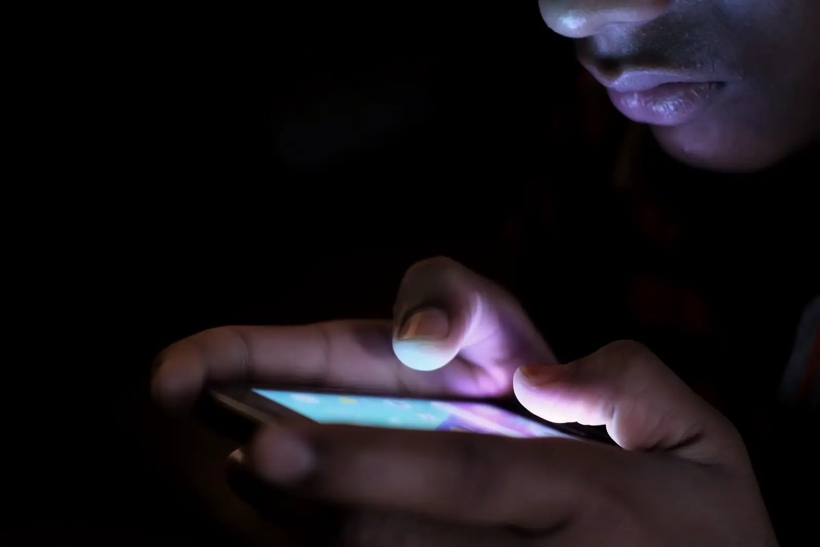 Hands holding a glowing phone in the dark